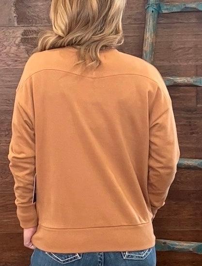 A person viewed from behind wearing a camel-colored long-sleeve sweatshirt and blue jeans, standing in front of a rustic wooden wall with a weathered blue ladder.