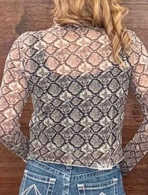 A woman viewed from the back wearing a sheer long-sleeve top with a snakeskin-style pattern in beige, brown, and gray, paired with blue jeans against a wooden background.
