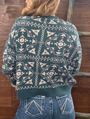 A person viewed from behind wearing a dark teal cropped sweater with a cream geometric and floral pattern, paired with blue jeans. 