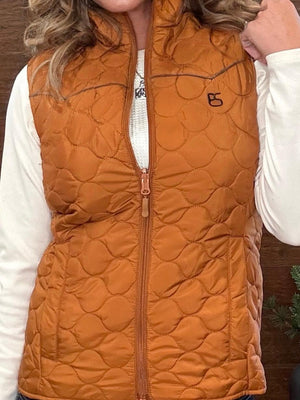 A woman wearing a quilted orange-brown zip-front vest over a white long-sleeve shirt. The vest has a small black embroidered logo on the left chest and a tonal zipper.