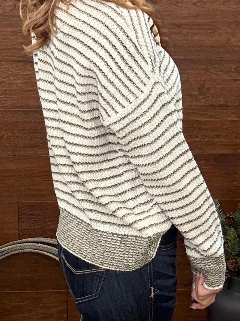 A woman wearing a cream and olive  horizontally striped knit sweater, shown from a side-back angle against a dark wood-paneled wall.