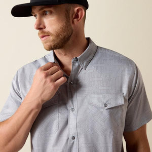 Man wearing a gray patterned shirt and black cap against a beige background