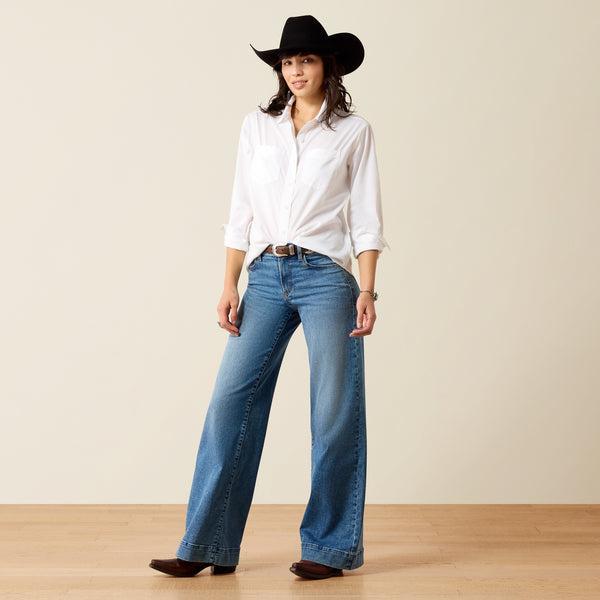 A woman wearing a white long-sleeve button-up shirt and a burgundy cowboy hat, looking down against a plain beige background.