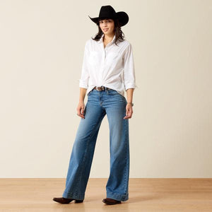 A woman wearing a white long-sleeve button-up shirt and a burgundy cowboy hat, looking down against a plain beige background.
