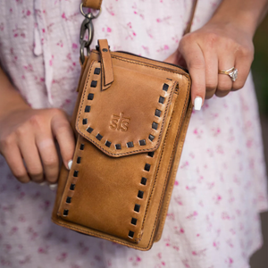 Brown leather wallet with decorative stitching held by a person wearing a floral dress.