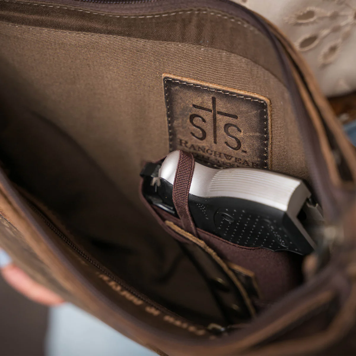 Brown leather bag with 'sts Ranchwear' logo, showing a gun inside.