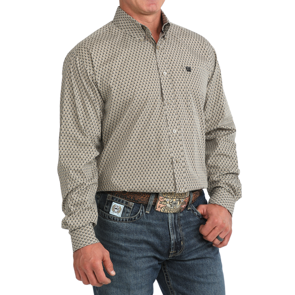 A man wearing a long-sleeve button-down shirt with a small repeating geometric pattern in beige and black, paired with blue jeans and a patterned belt.