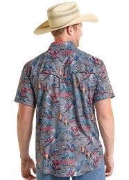Man wearing a patterned shirt and cowboy hat, standing outdoors.