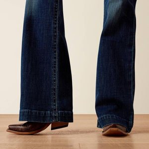 Close-up of blue jeans and brown shoes on a wooden floor with a beige wall background