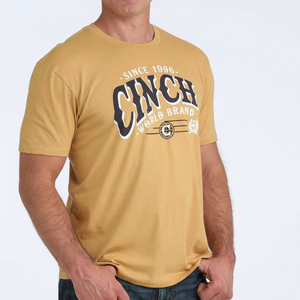 Man wearing a mustard yellow t-shirt with 'Cinch World Brand' logo on a light gray background