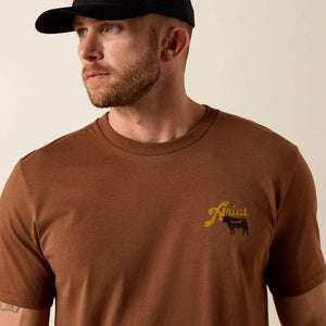 Man wearing a brown Ariat t-shirt with yellow text and a cow graphic on the back.