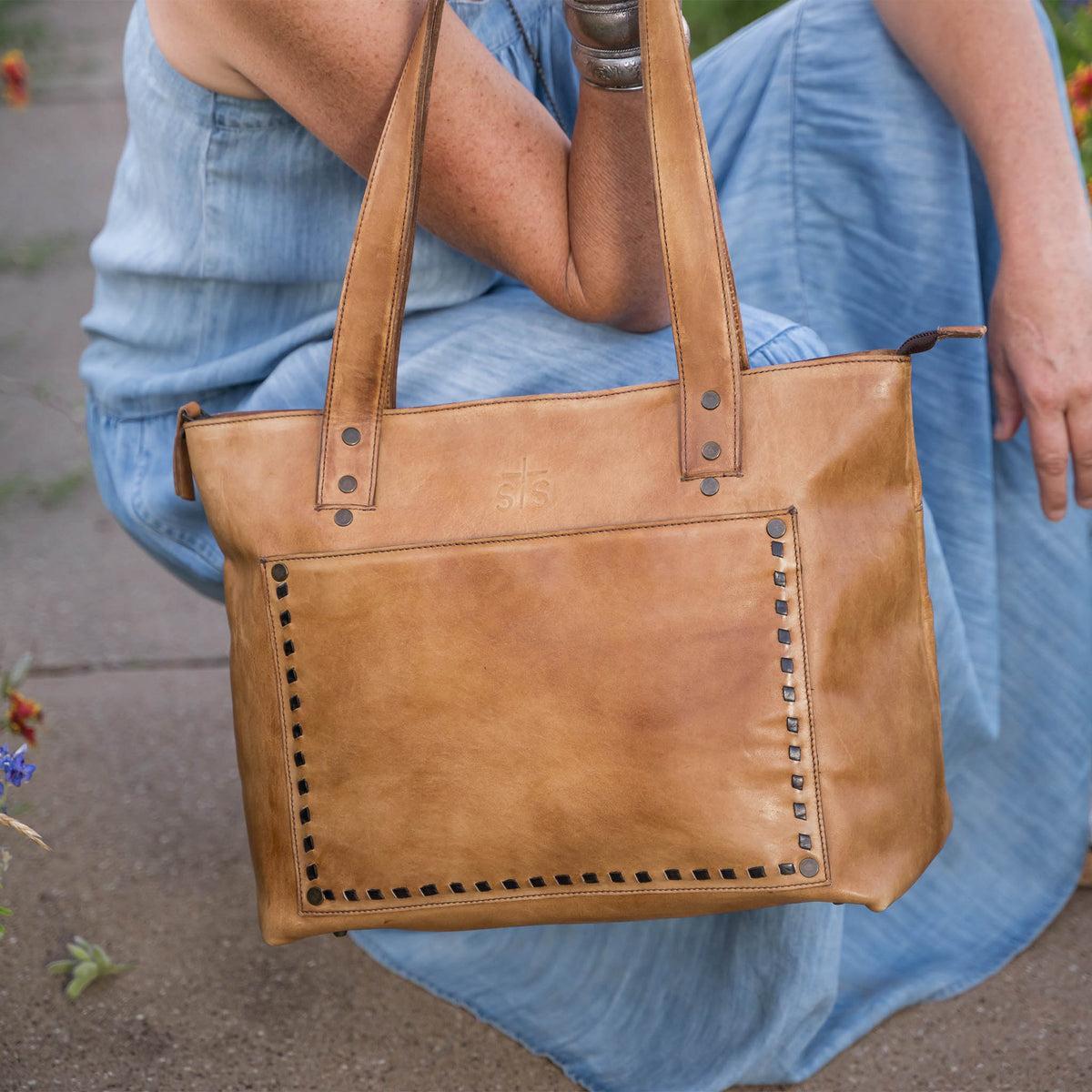 Brown leather tote bag held by a person wearing a blue dress.