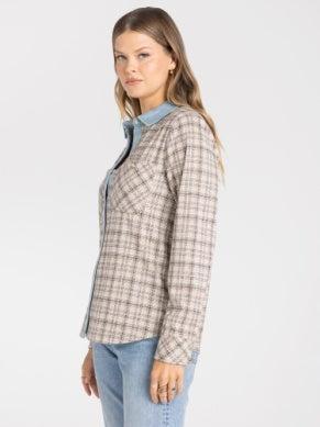A woman wearing a beige and brown plaid button-up shirt jacket over a light blue collared shirt, paired with light blue jeans, photographed against a plain light gray background.