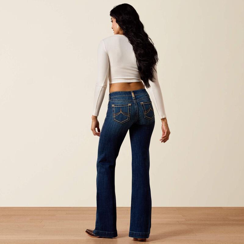 Woman wearing blue jeans and a white long-sleeve top on a plain background
