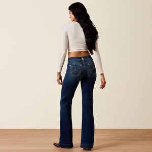 Woman wearing blue jeans and a white long-sleeve top on a plain background