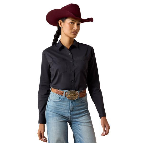 A woman wearing a black long-sleeve button-up shirt and a burgundy cowboy hat, looking down against a plain beige background.