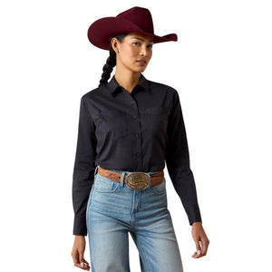 A woman wearing a black long-sleeve button-up shirt and a burgundy cowboy hat, looking down against a plain beige background.