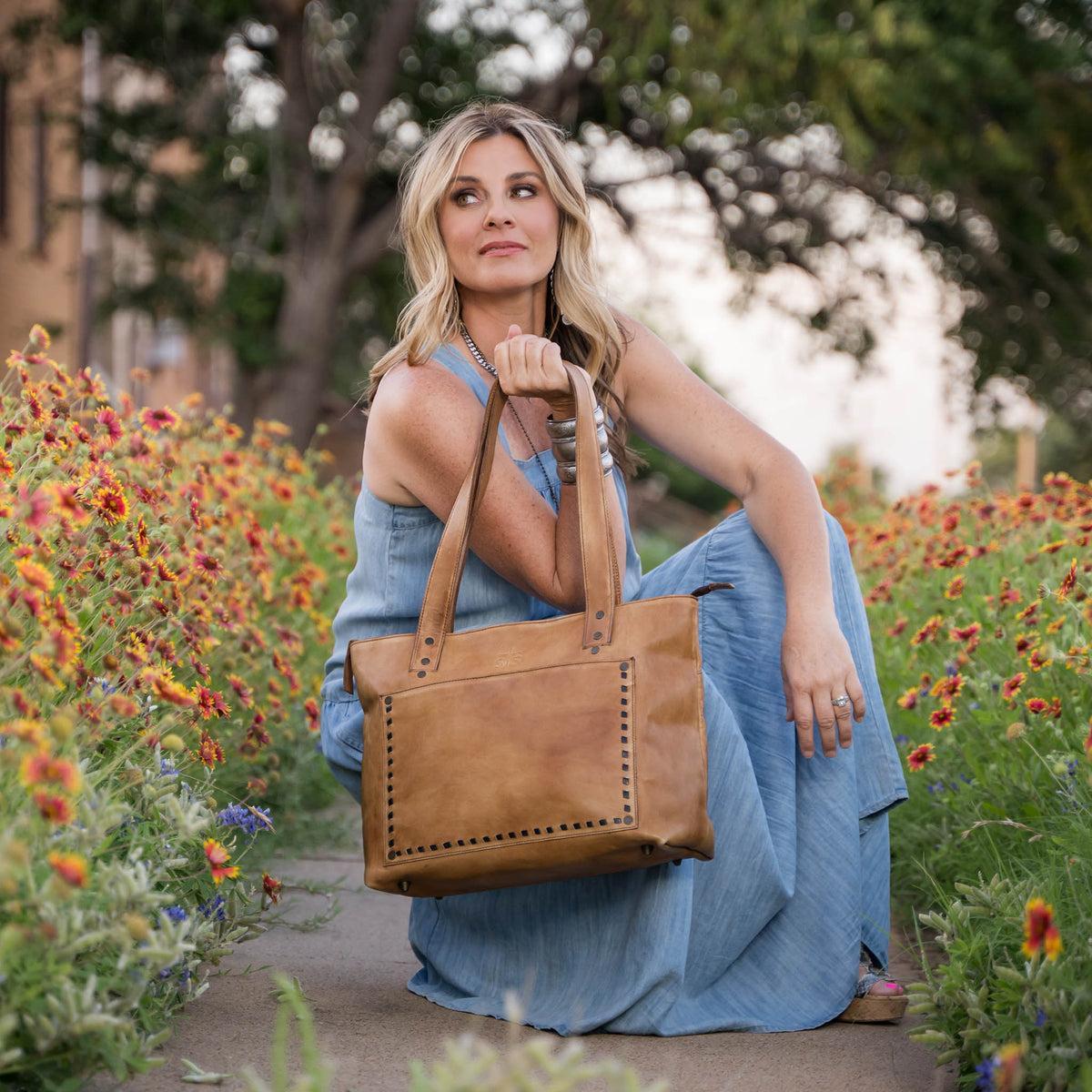 Woman in a blue dress holding a brown leather bag in a garden setting