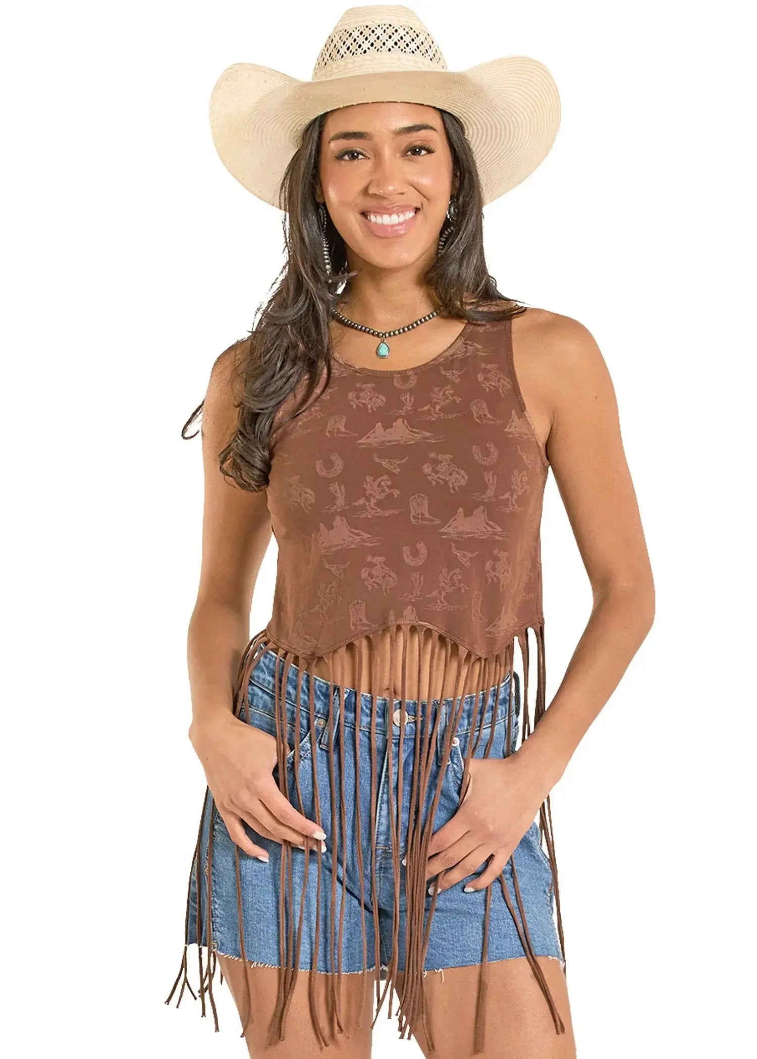 Woman wearing a brown patterned tank top with fringes and a blue denim skirt, paired with a beige cowboy hat on a white background.