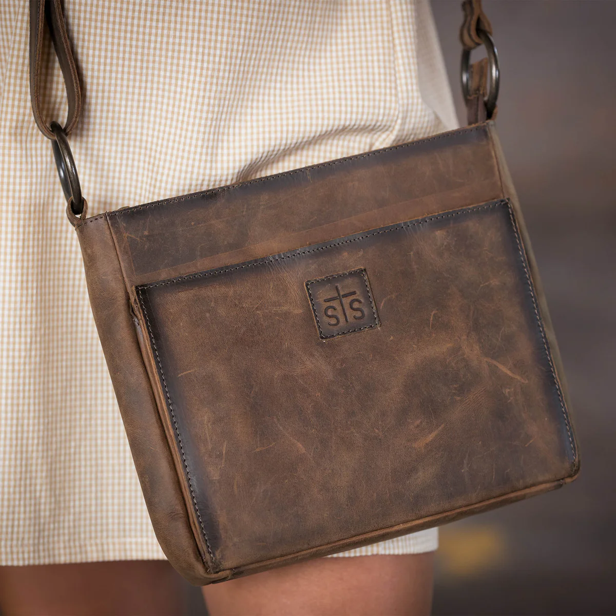 Brown leather bag with a visible brand logo worn by a person.