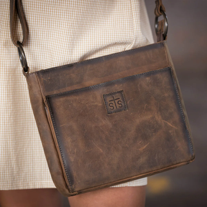 Brown leather bag with a visible brand logo worn by a person.