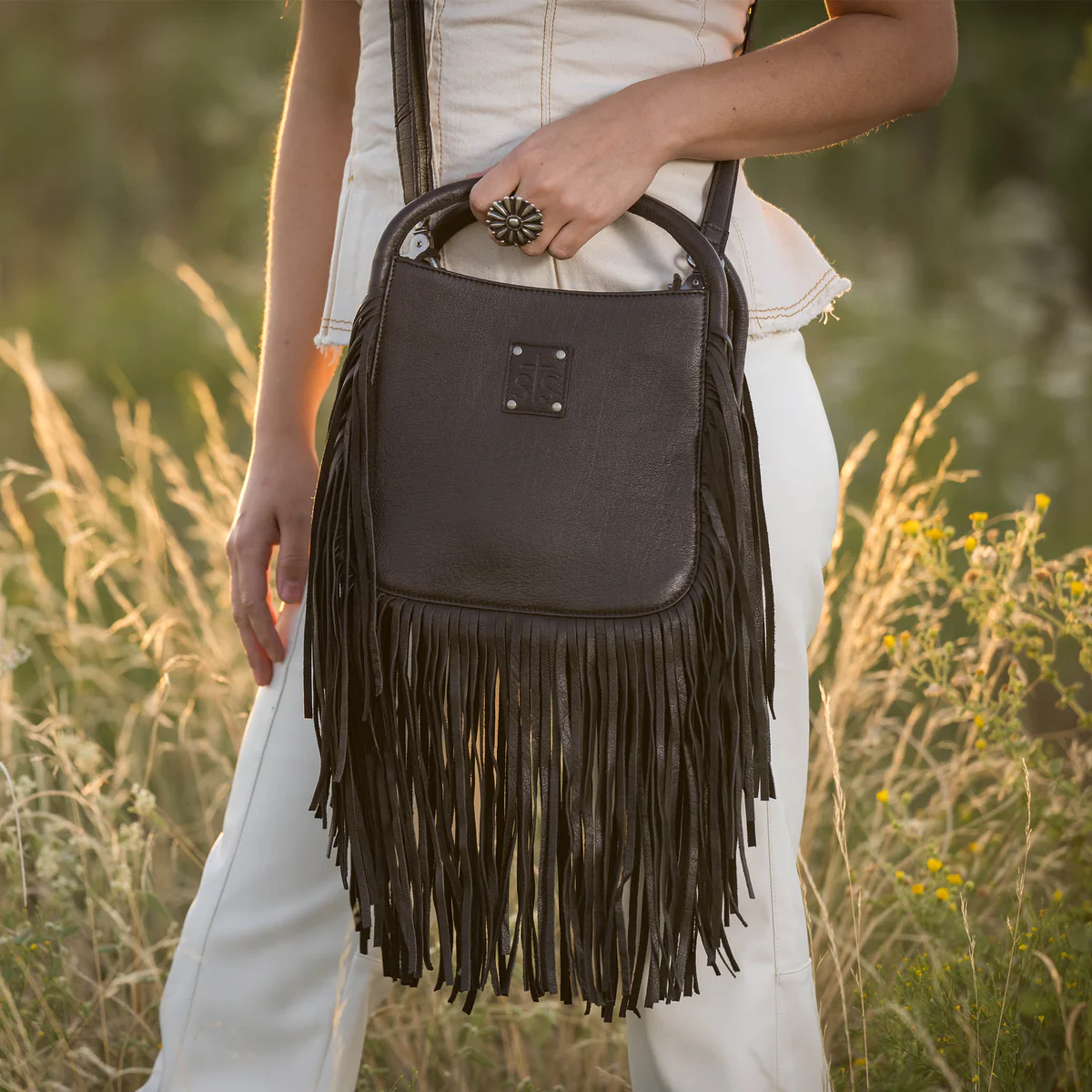 Person holding a black fringed handbag in a natural setting