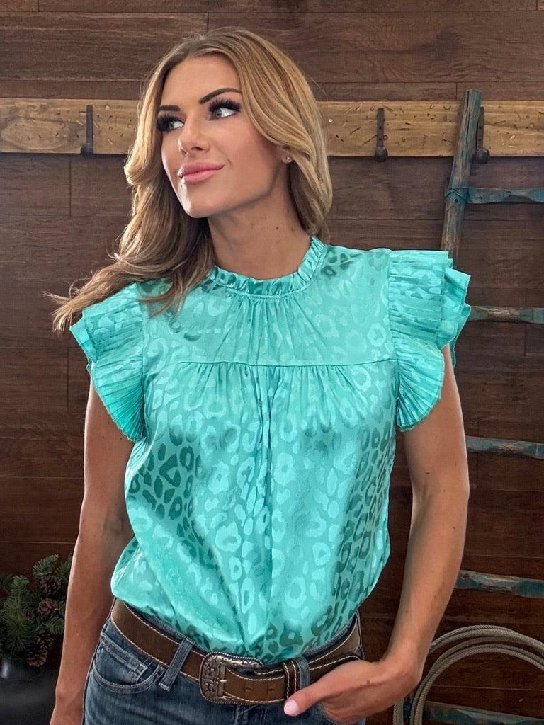 Woman wearing a teal blouse with ruffled sleeves against a wooden background