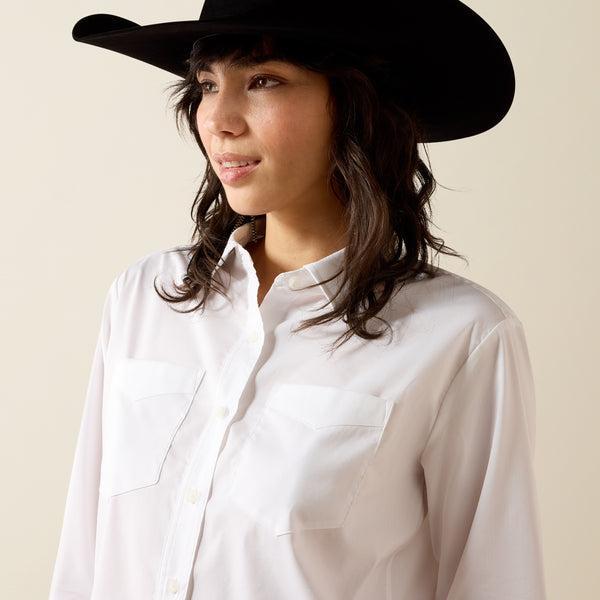 A woman wearing a white long-sleeve button-up shirt and a burgundy cowboy hat, looking down against a plain beige background.
