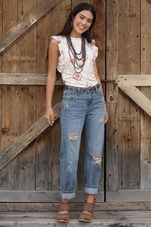 Woman wearing a white floral top and blue jeans standing in front of a wooden door.