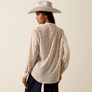 Woman wearing a patterned blouse and wide-brimmed hat against a beige background