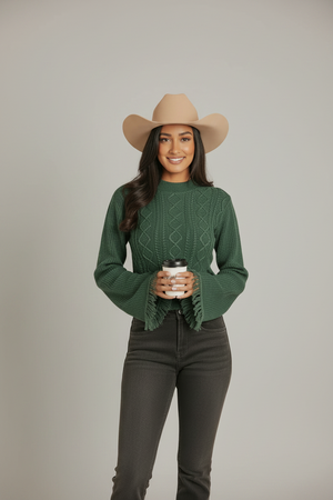 A woman wearing a green cable-knit cropped sweater with fringed bell sleeves. 