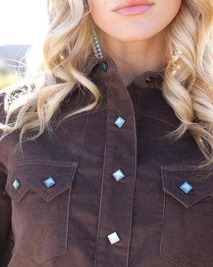 Close-up of a woman wearing a dark brown corduroy button-up shirt jacket with decorative light blue and white diamond-shaped studs on the chest pockets and front placket.