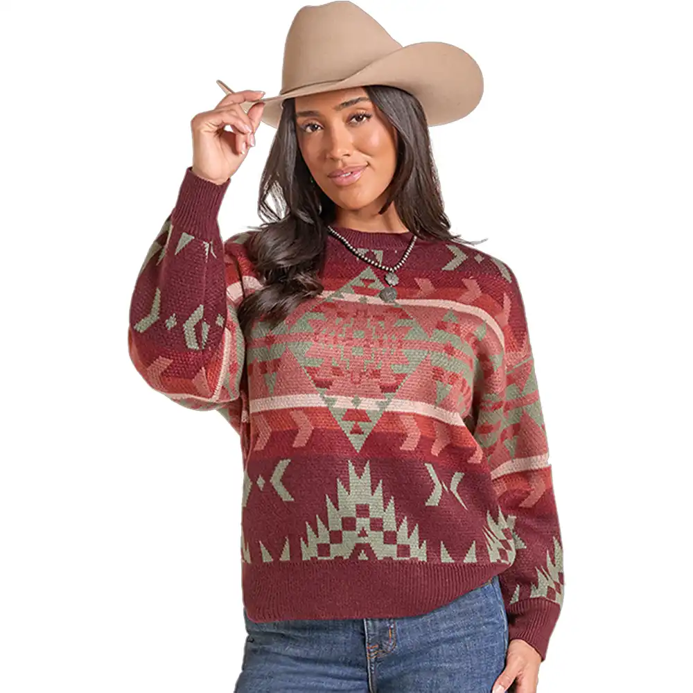 A woman wearing a long-sleeve knit sweater with a Southwestern geometric pattern in burgundy, sage green, and beige, paired with a tan cowboy hat and blue jeans, against a solid white background.
