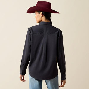 A woman wearing a black long-sleeve button-up shirt and a burgundy cowboy hat, looking down against a plain beige background.