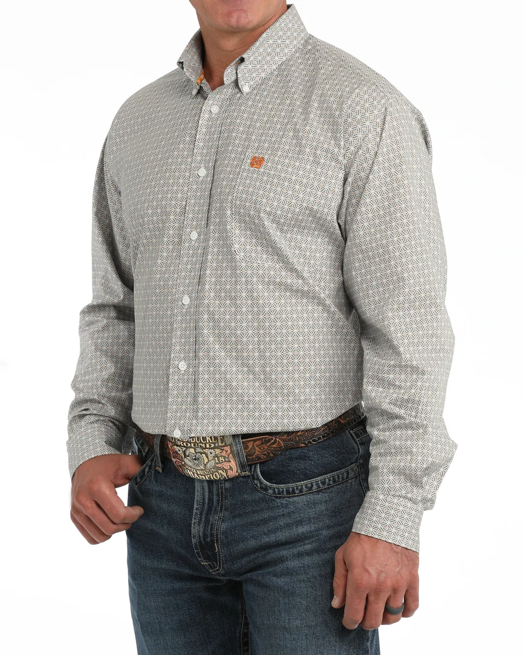 A man wearing a liwhite micro-patterned button-down shirt with a small orange logo on the chest, tucked into blue jeans with a western belt.