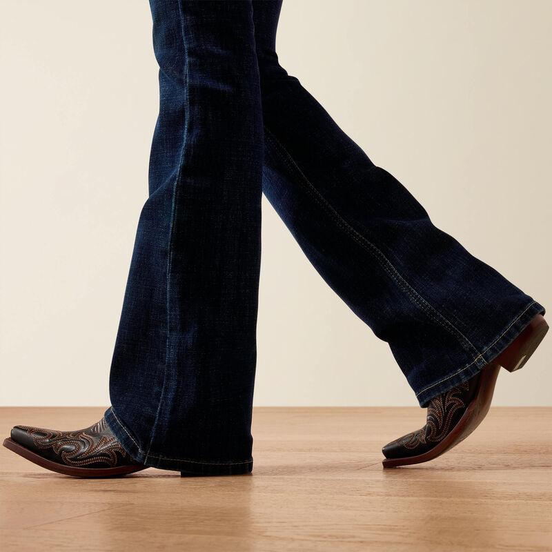 Person wearing blue jeans and brown cowboy boots on a wooden floor.