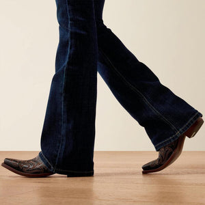 Person wearing blue jeans and brown cowboy boots on a wooden floor.