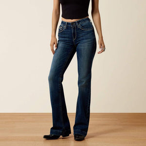 A model wearing a pair of dark blue high-waisted flare jeans, paired with a black ribbed crop top and black shoes, standing against a neutral beige wall and light wood floor.