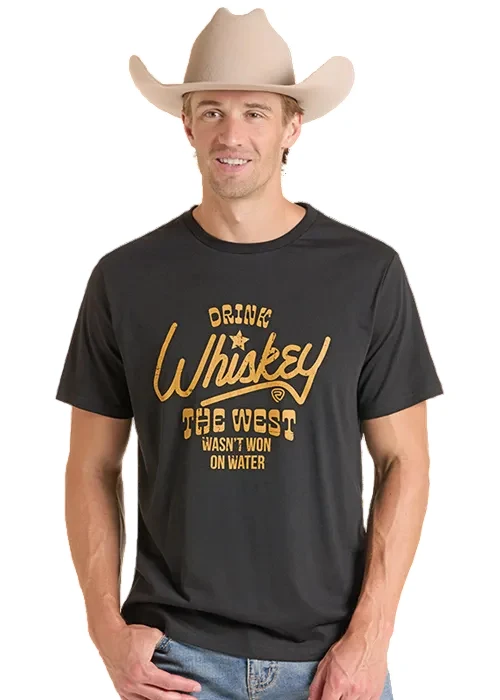 A man wearing a black graphic t-shirt and a beige cowboy hat, standing against a plain white background. The t-shirt features a gold-colored graphic that reads 'DRINK Whiskey THE WEST WASN'T WON ON WATER'.