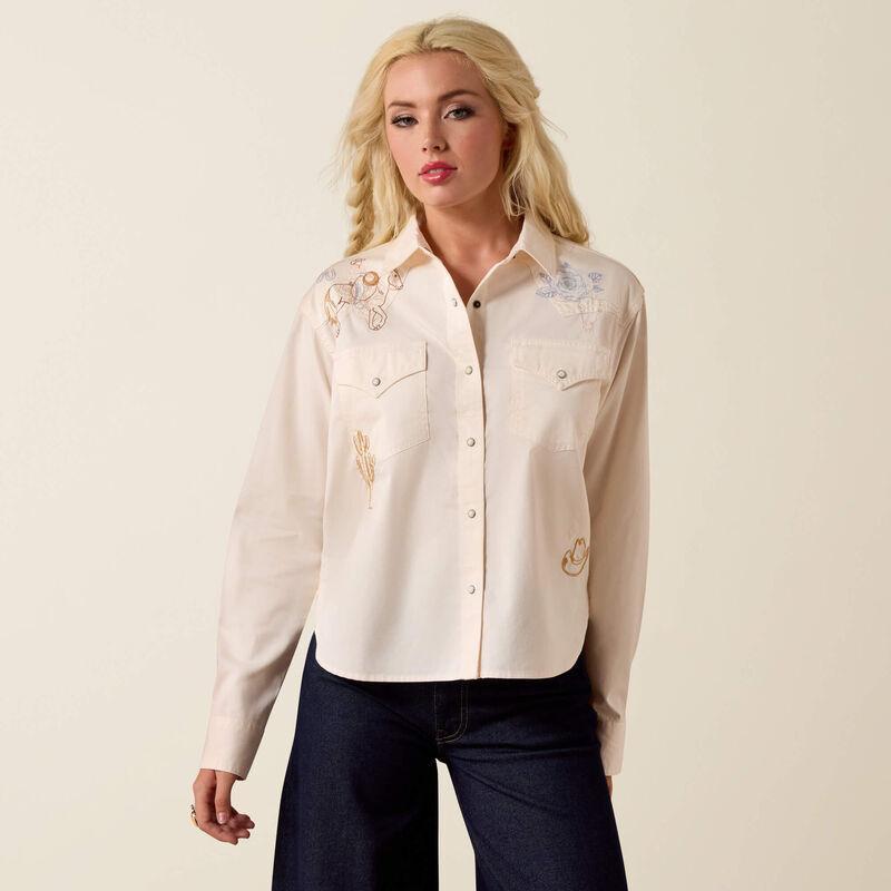 Woman wearing a cream-colored embroidered shirt against a beige background