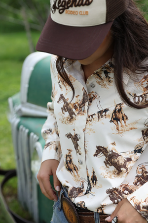 Person wearing a cowboy hat and shirt with horse and rider pattern, standing in front of a vintage truck.