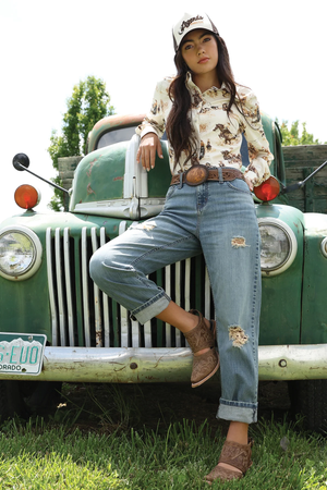Woman posing in front of a vintage green truck wearing a patterned shirt, jeans, and a cap.