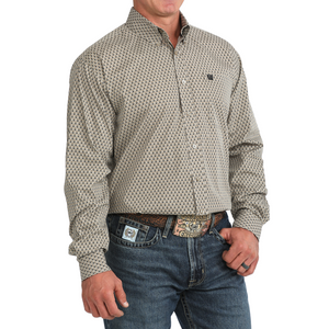 A man wearing a long-sleeve button-down shirt with a small repeating geometric pattern in beige and black, paired with blue jeans and a patterned belt.