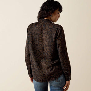 A woman shown from the back wearing a dark brown long-sleeve button-up shirt with an intricate gold baroque-style pattern. 