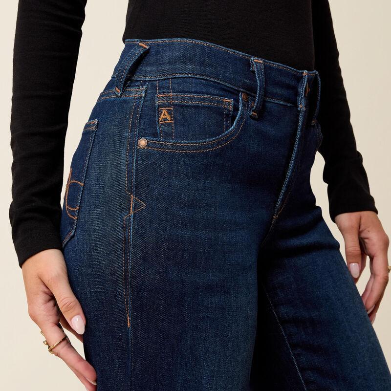 Close-up of a person wearing dark blue denim jeans with a black long-sleeve top, showing the back pocket and waistband details against a light beige background.