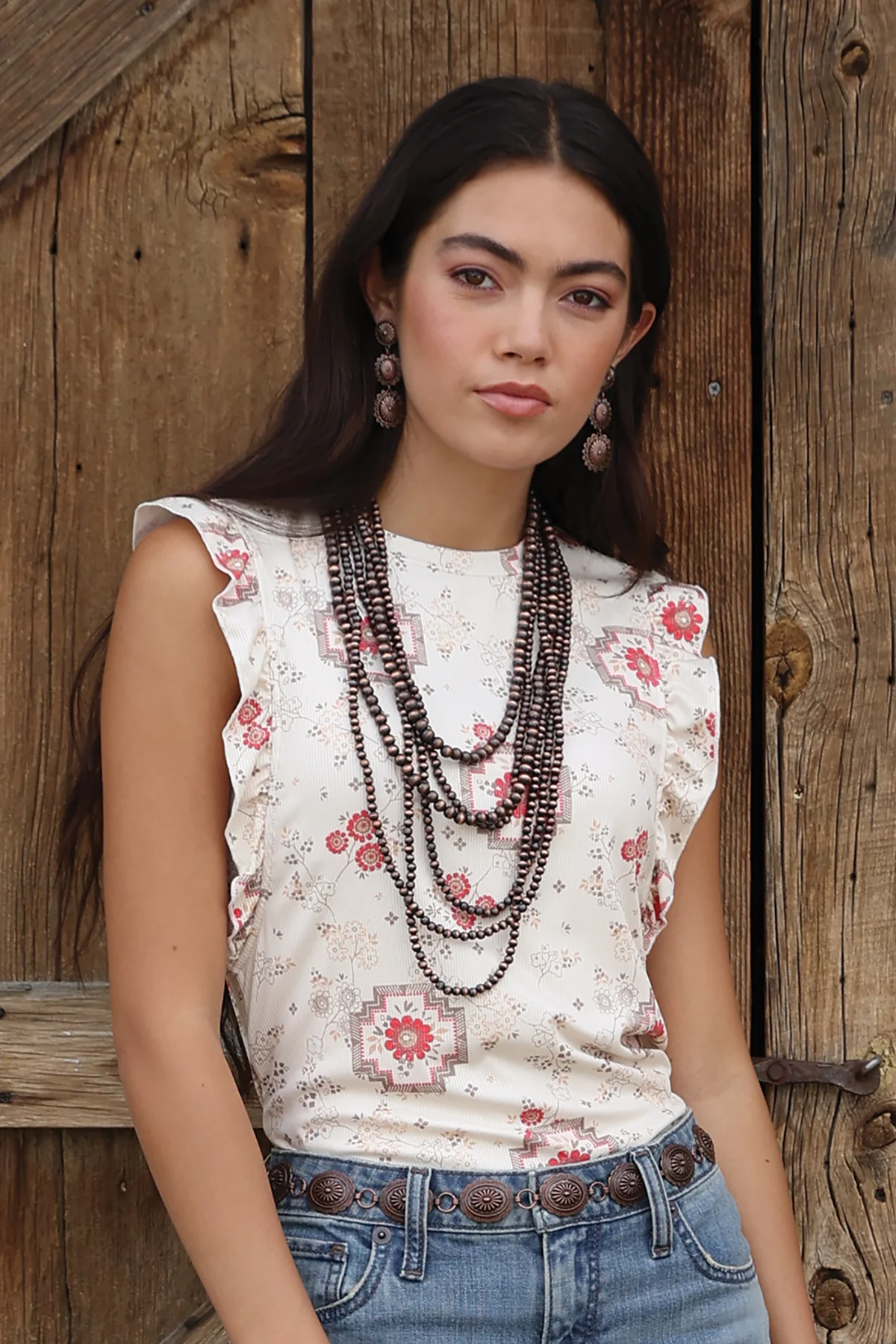 Woman wearing a floral sleeveless top and blue jeans against a wooden background