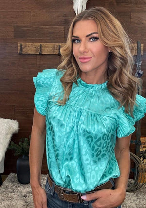 Woman wearing a teal blouse with ruffled sleeves in a rustic setting