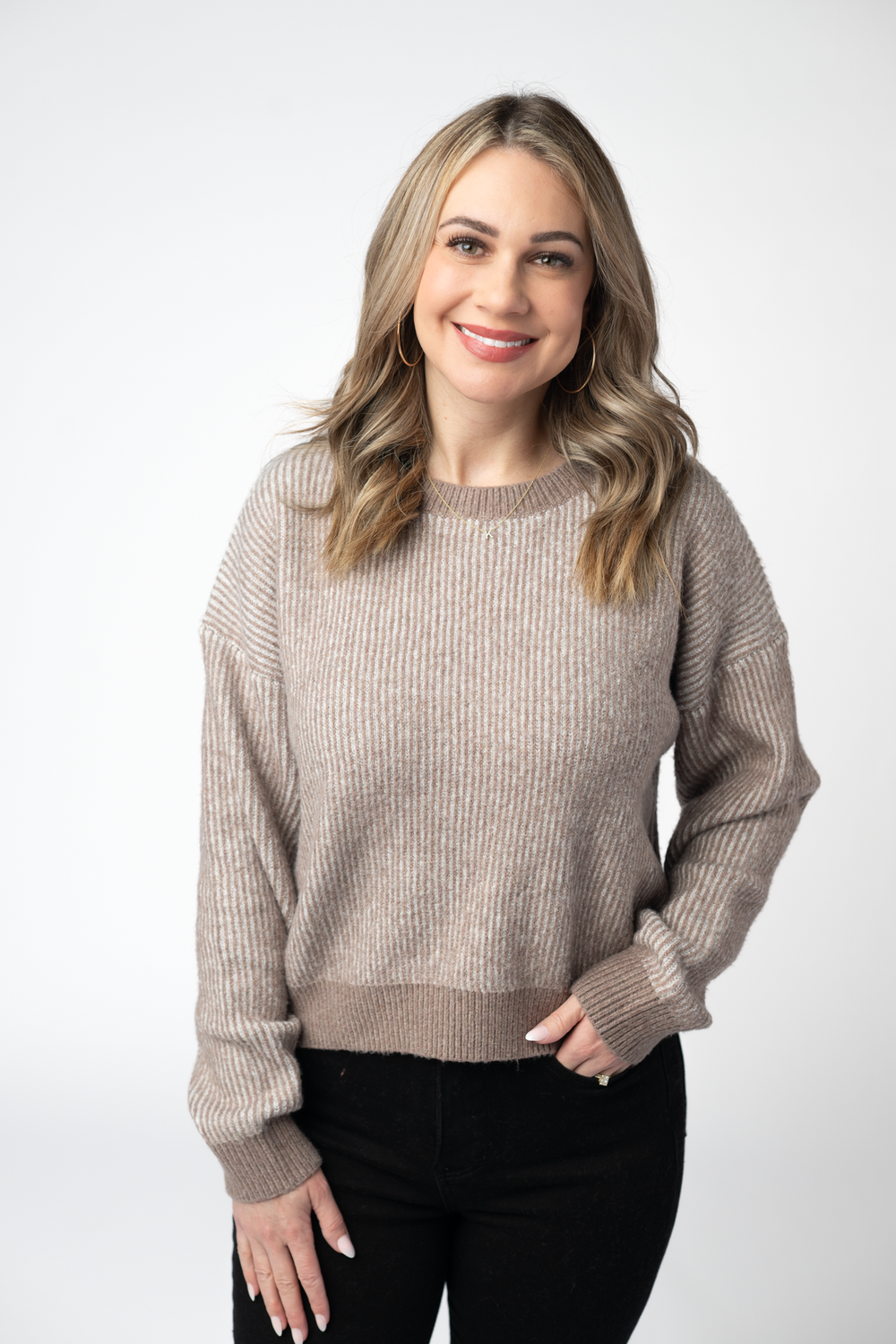 A woman wearing a beige ribbed knit crewneck sweater 