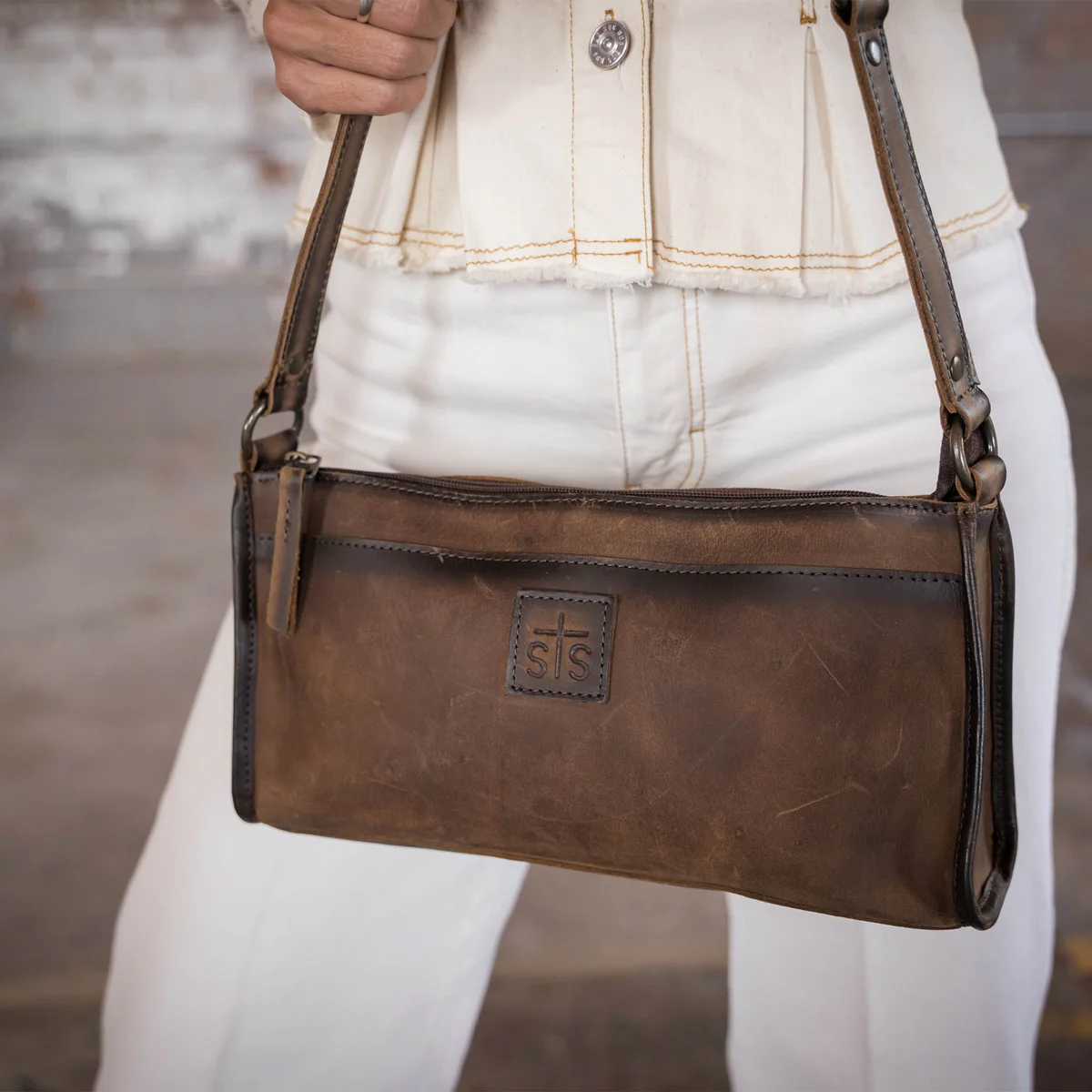 Brown leather handbag held by a person wearing a white jacket and pants.