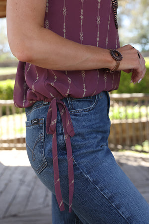Woman wearing a mauve top with a pattern and blue jeans.